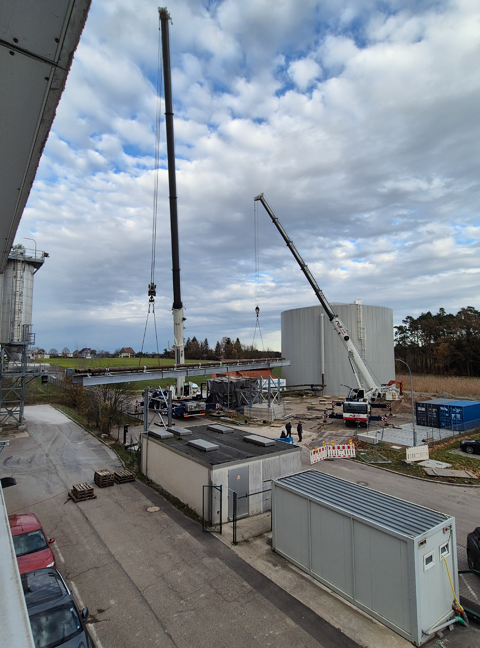 Zwei Kräne heben Materialien auf einer Baustelle mit einem großen Lagerbehälter im Hintergrund. TEAtherm in Dinkelsbühl