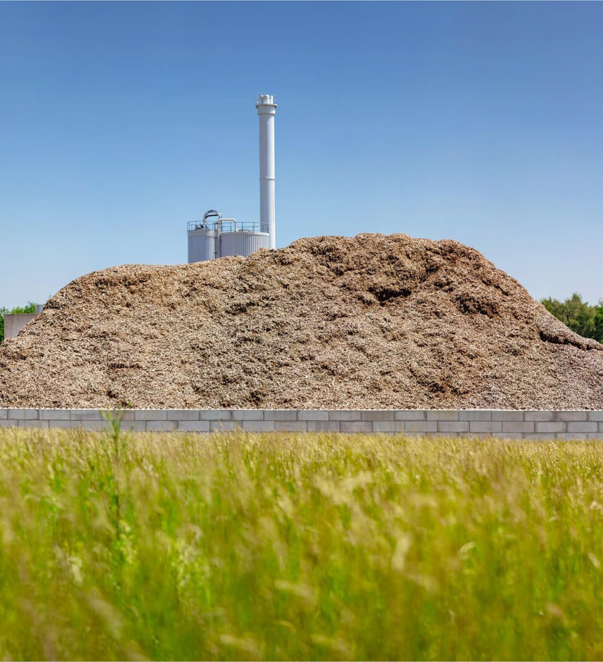 Großer Haufen von Biomasse mit einem Schornstein im Hintergrund unter klarem Himmel. TEAtherm in Dinkelsbühl